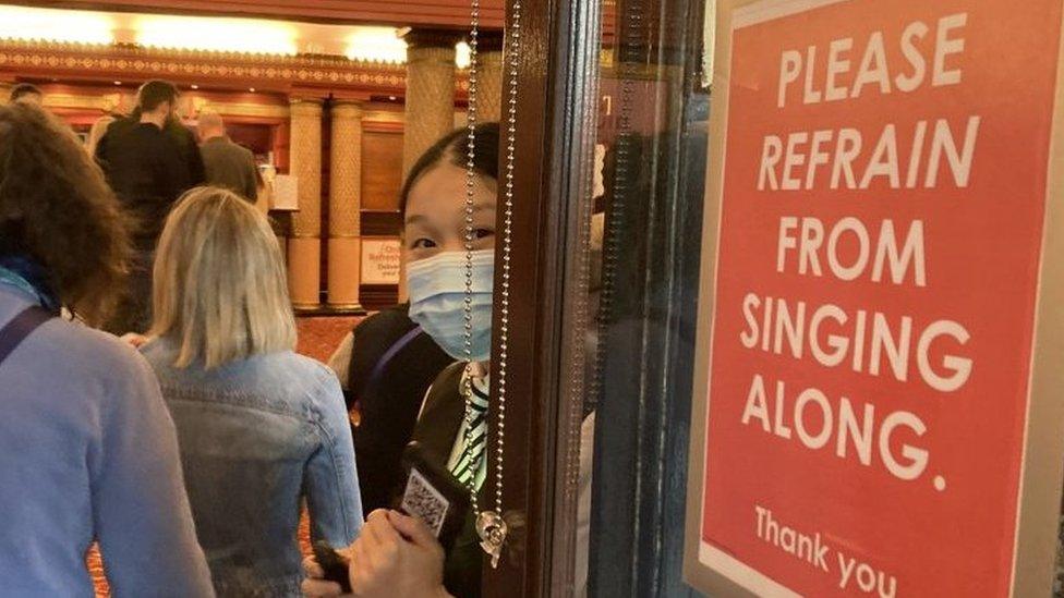 Theatre-goers walk past a sign in the theatre entrance that reads "Please refrain from singing along".