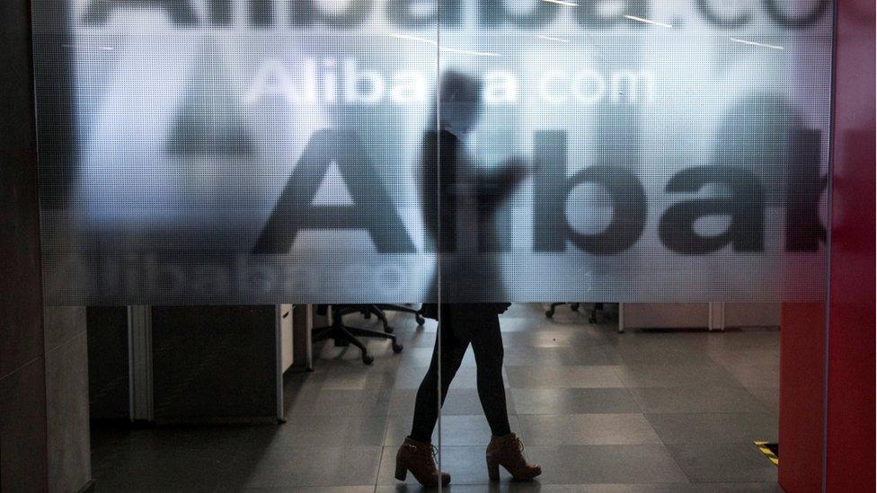 An employee is seen behind a glass wall with the logo of Alibaba at the company's headquarters on the outskirts of Hangzhou, Zhejiang province, 23 April 2014.