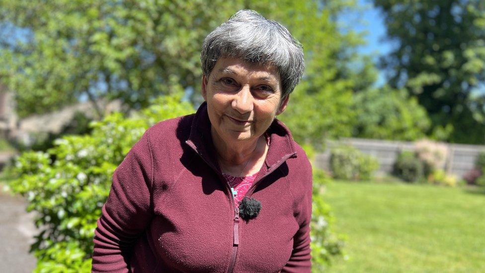 Janet Hazelwood wearing a purple fleece and standing in the garden