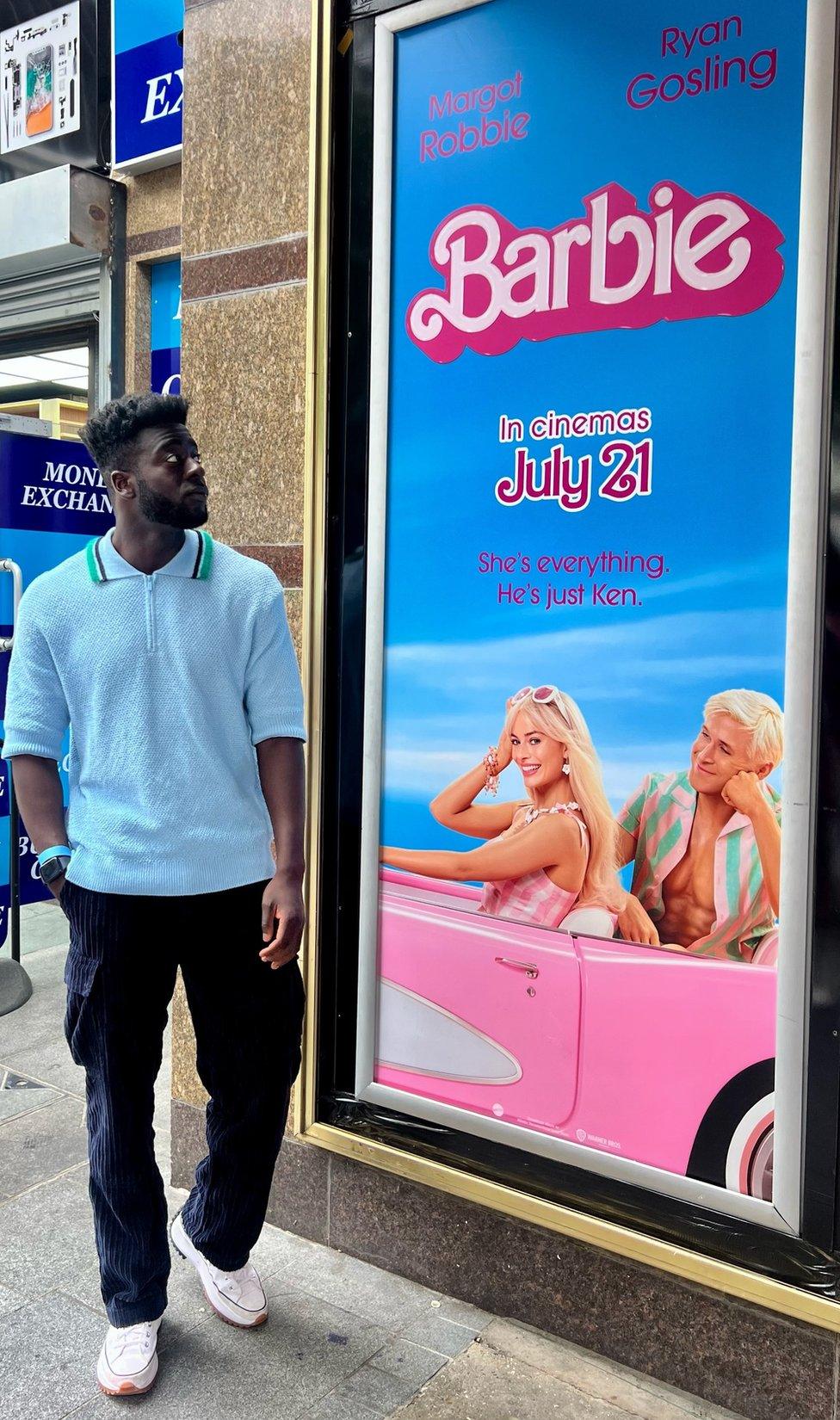 Gustave Die looking at a Barbie billboard