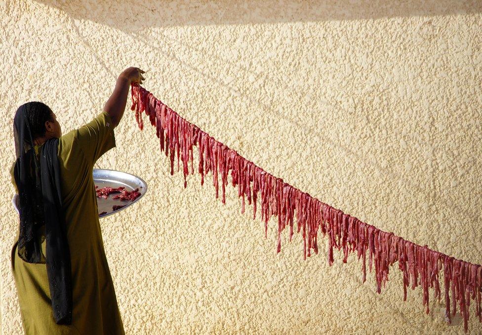 A woman hangs raw beef on a line outside