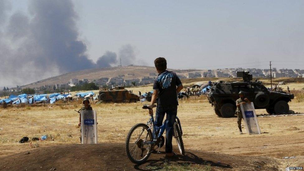 A boy on a bike watches smoke over the Syrian town of Kobane from Turkish territory, 27 June