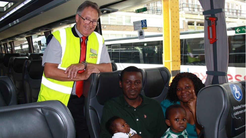 The driver stands above the family, who are sitting on a coach