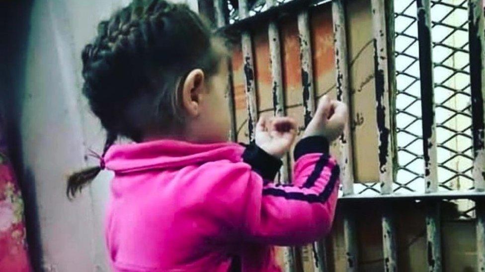 A child sits by a barred window in prison