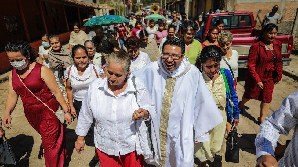 Miguel Pantaleon smiling with a procession of locals on a street