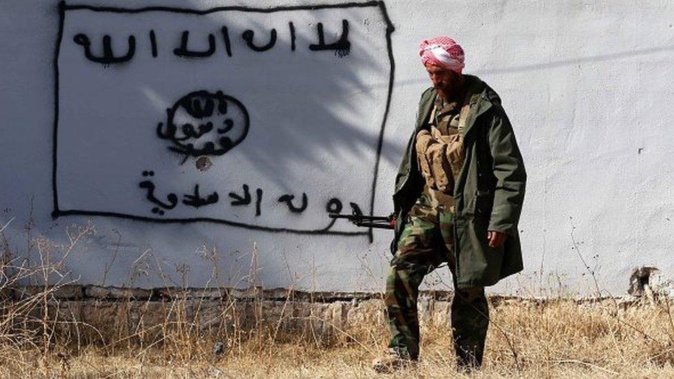 A Kurdish fighter walks by a wall bearing a drawing of the flag of the Islamic State (IS) group in the northern Iraqi town of Sinjar, in the Nineveh Province, on November 13, 2015.