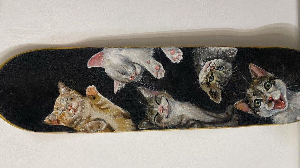 A skateboard painted with several cats with happy facial expressions