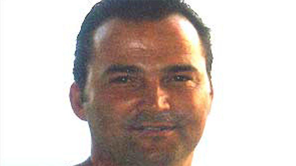 Stuart Campbell, who is tanned and has slicked back hair that is black. He has stubble and is smiling at the camera, in front of a white background