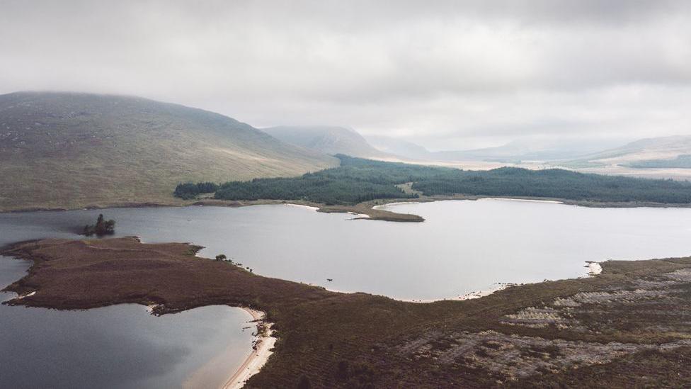 An aerial view of a loch on a grey cloudy day with hills in the distance