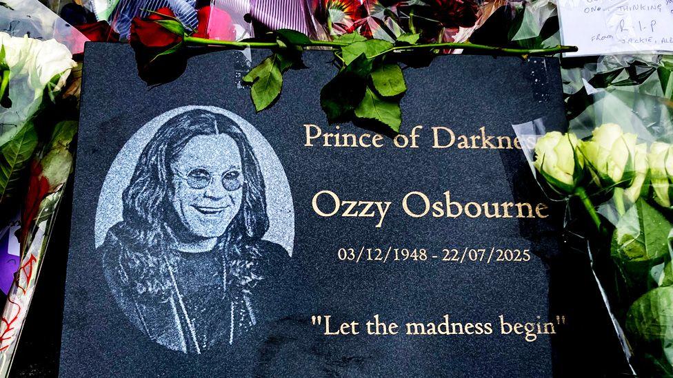 A plaque with a picture of Ozzy and the words "Princde of Darkness Ozzy Osbourne 03/12/1948-22/07/2025 'Let the madness begin'"