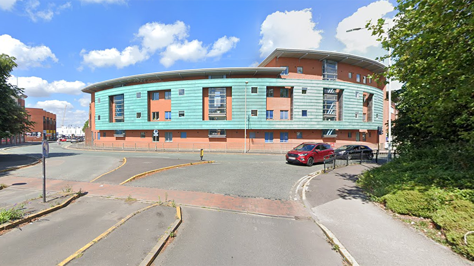 Google Streetview photo of the block of flats on St Georges Parade in Wolverhampton. Built around a tight corner in the road, the two to four-storey flats are built from red brick with light blue cladding