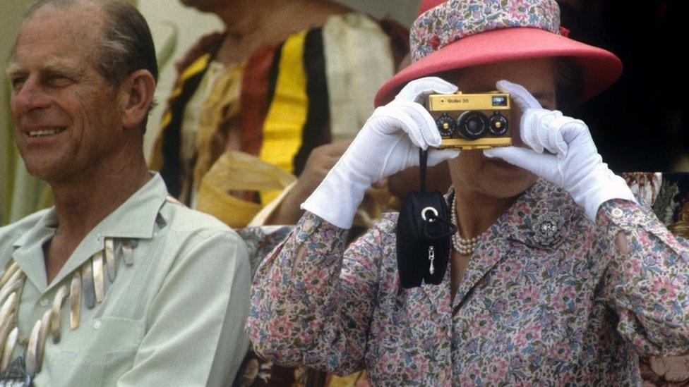 The Queen in Tuvalu in 1982 with the Duke of Edinburgh. She is taking a picture using a disposable camera.