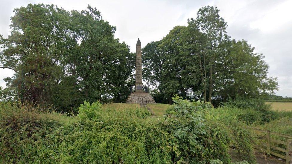 Stone obelisk with pointed top surrounded by trees