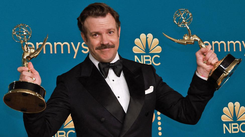 Ted Lasso star Jason Sudeikis holding up two Emmy Awards