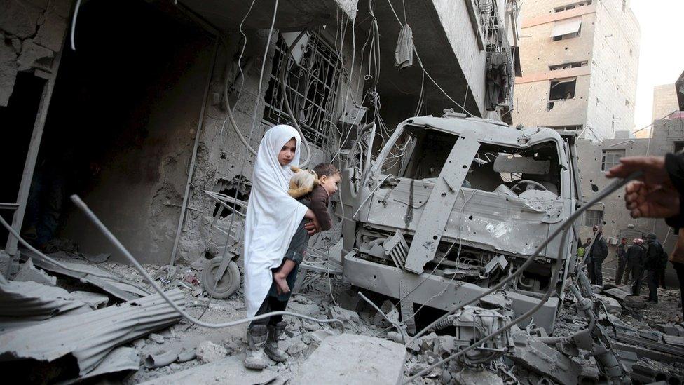 File photo: A girl carrying a baby inspects damage at a site in the town of Douma, eastern Ghouta in Damascus, Syria, 10 January 2016