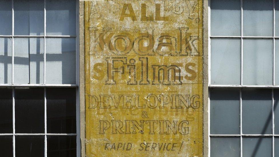 An old yellow painted Kodak film sign on a bath stone building in between Georgian-style windows