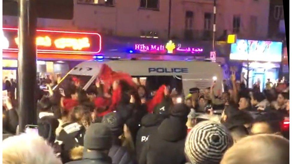 Moroccan fans gather around a police car holding flags