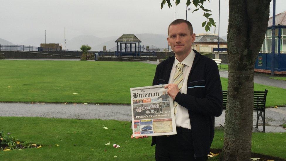 A man holds up a newspaper outside