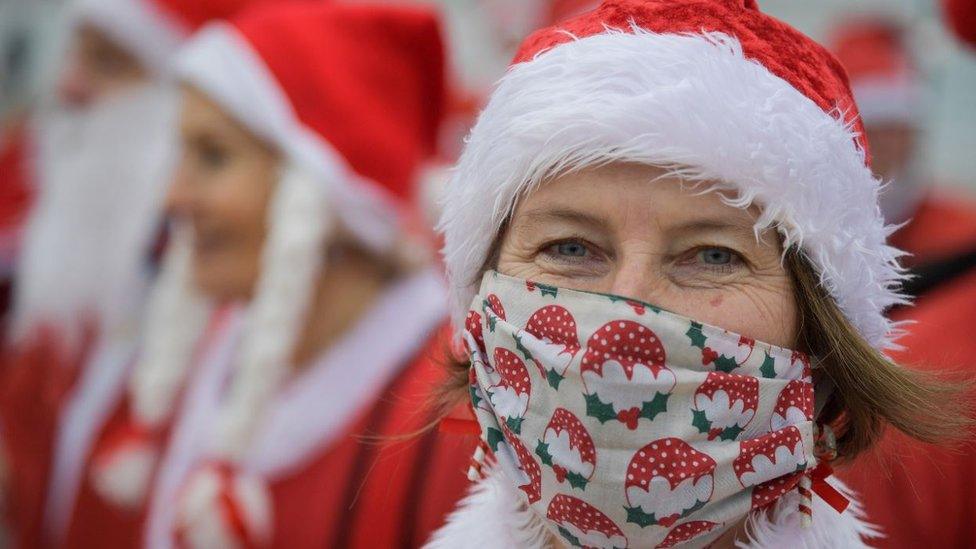 Woman dressed as Santa in a mask with Christmas puddings on it