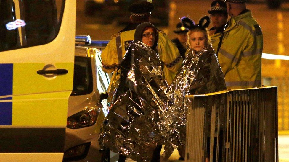 Two women wrapped in thermal blankets stand near the Manchester Arena, where US singer Ariana Grande had been performing