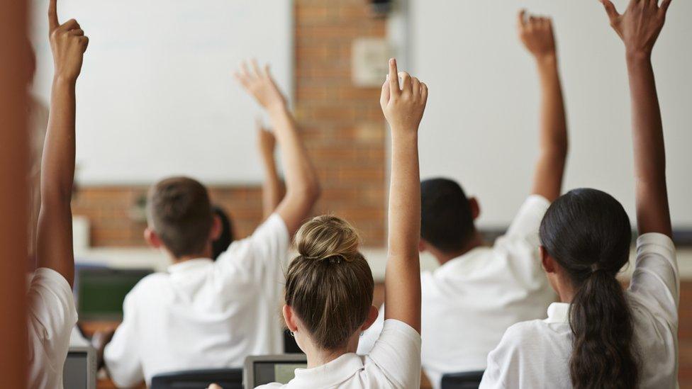 school students in white shirts with hands up