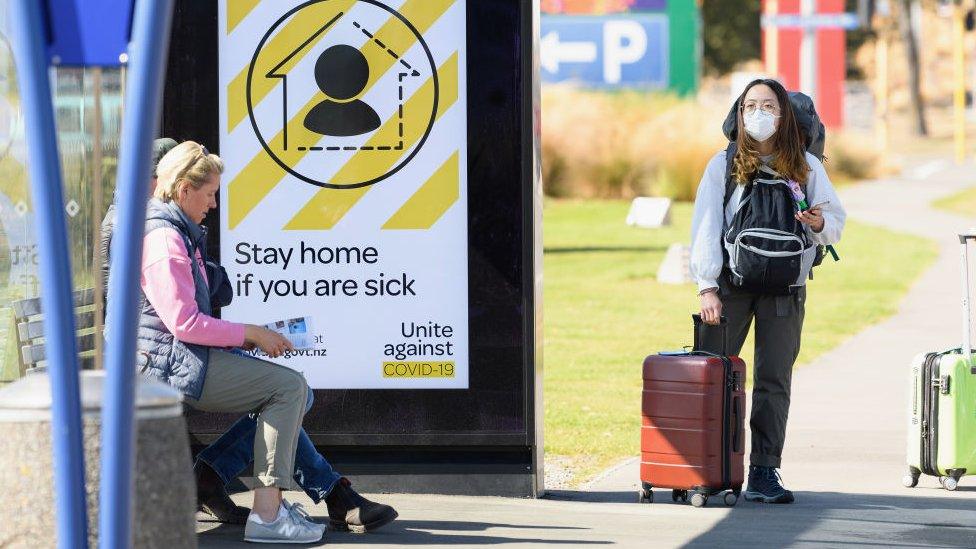 A traveller wearing a protective mask is seen waiting for a bus near Christchurch International Airport