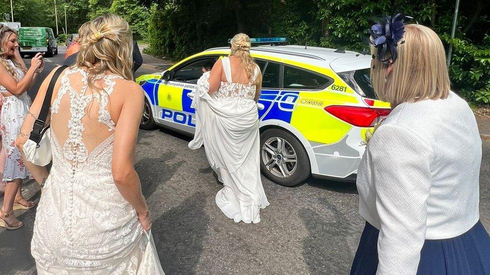 Jemma and Sian Batchelor-Thomas approaching the police car in their wedding dresses