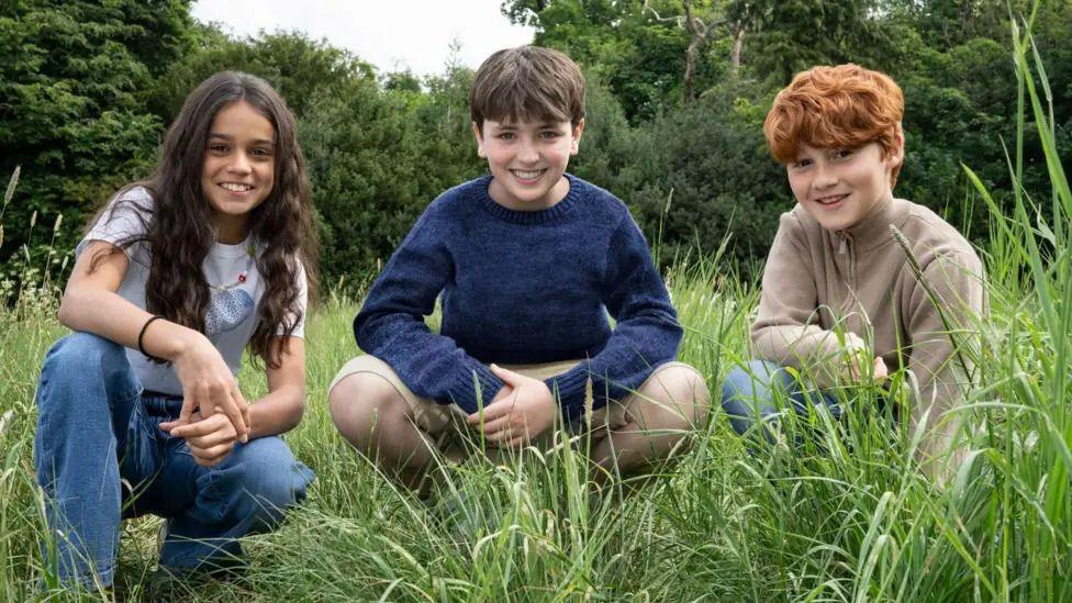 Arabella Stanton, Dominic McLaughlin and Alastair Stout sitting in some grass
