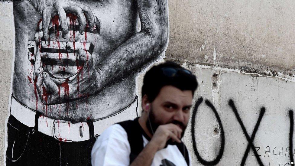 A man in Athens passes by a graffiti showing a euro sign bleeding