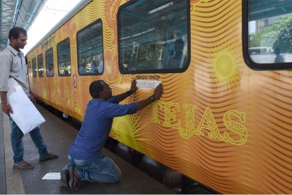 In this photograph taken on May 21, 2017, Indian staff paste stickers below an emergency window of the Tejas Express luxury train before its first journey between Mumbai and Goa at the Chattrapati Shivaji Terminus terminus station in Mumbai.