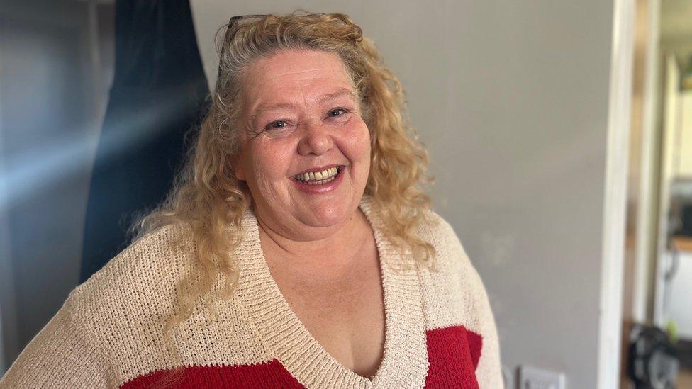 a woman in a house smiling at the camera, wearing a white and red cardigan