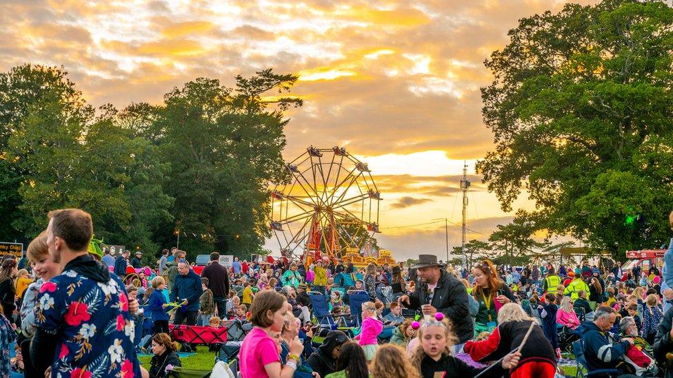 Revellers at Camp Bestival at sunset with a big wheel in the background