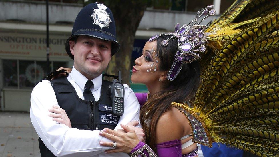 A performer in a costume poses by a policeman at Notting Hill Carnival