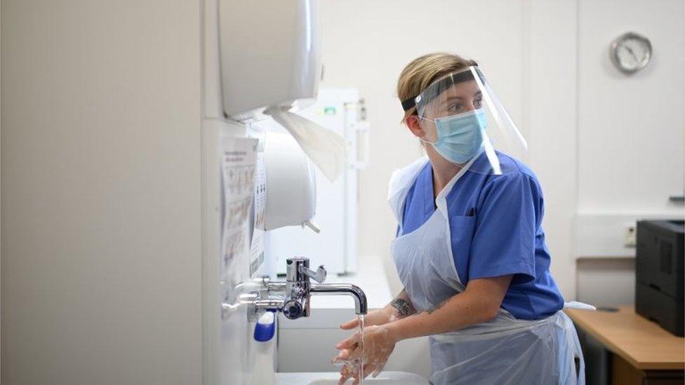 A nurse in PPE washes her hands at a primary care centre