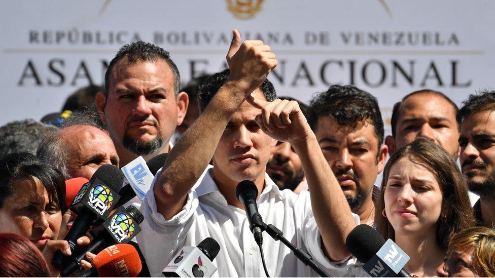 Venezuela's National Assembly president Juan Guaido points at his wrist as he speaks before a crowd of opposition supporters during an open meeting in Vargas