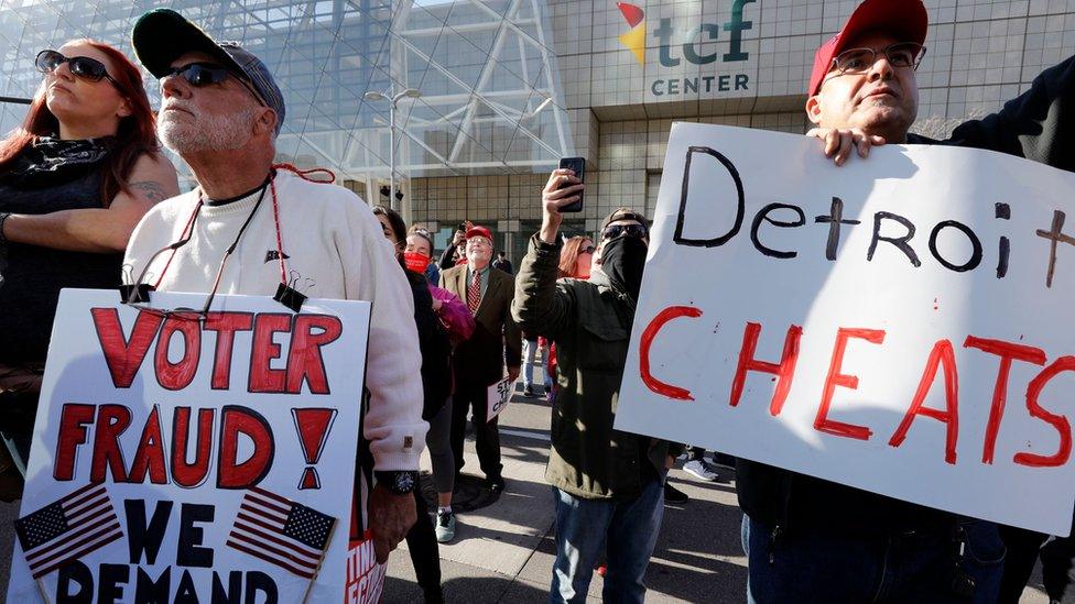 Two male protesters in Michigan hold signs claiming voter fraud. One reads "Voter fraud" and other other "Detroit cheats".