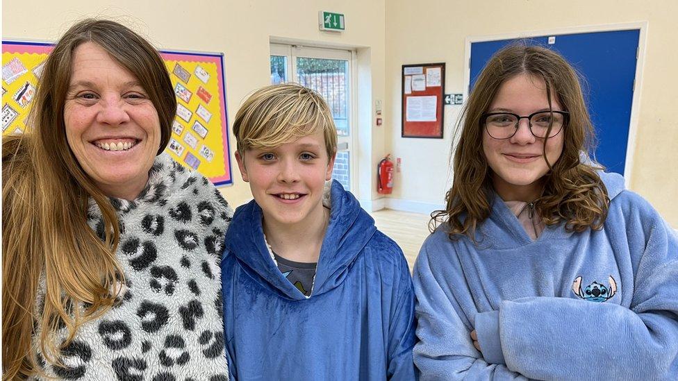 A woman with long brown hair wearing black and white pyjamas and a boy and girl in blue pyjamas