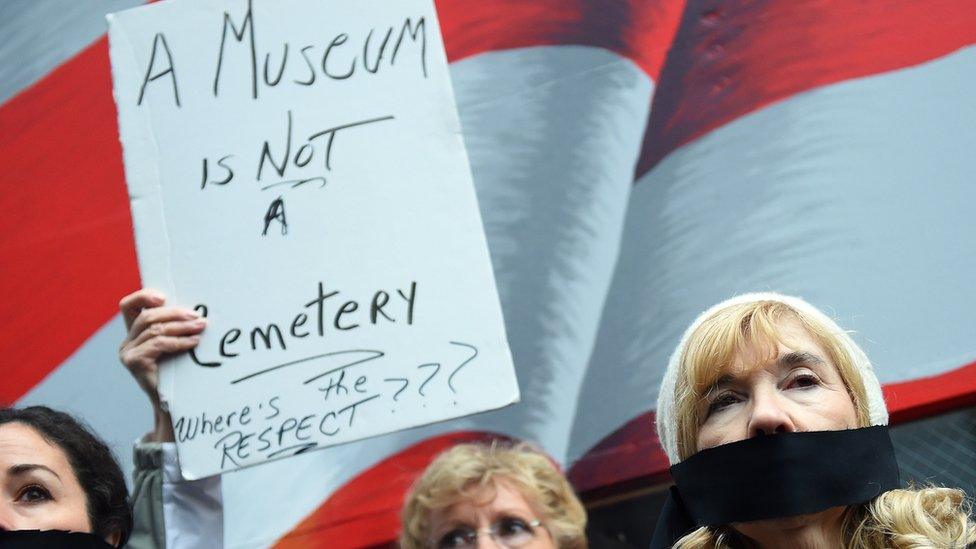 Protestors hold a "museum is not a cemetery" sign in protest