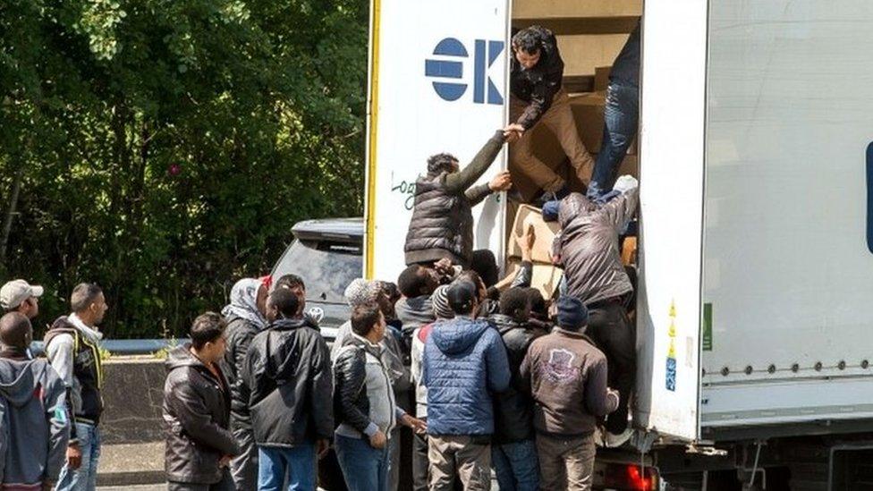 Migrants climb in the back of a lorry on the highway leading to the Eurotunnel