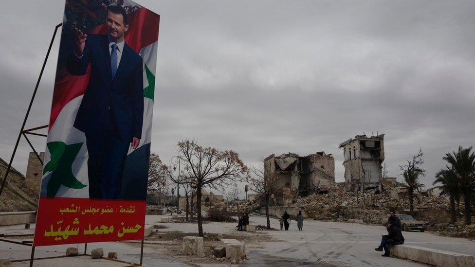 A brightly-coloured poster of President Assad stands in front of ruined buildings in Aleppo