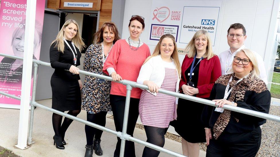 Five women and a man stand outside a small medical-looking building