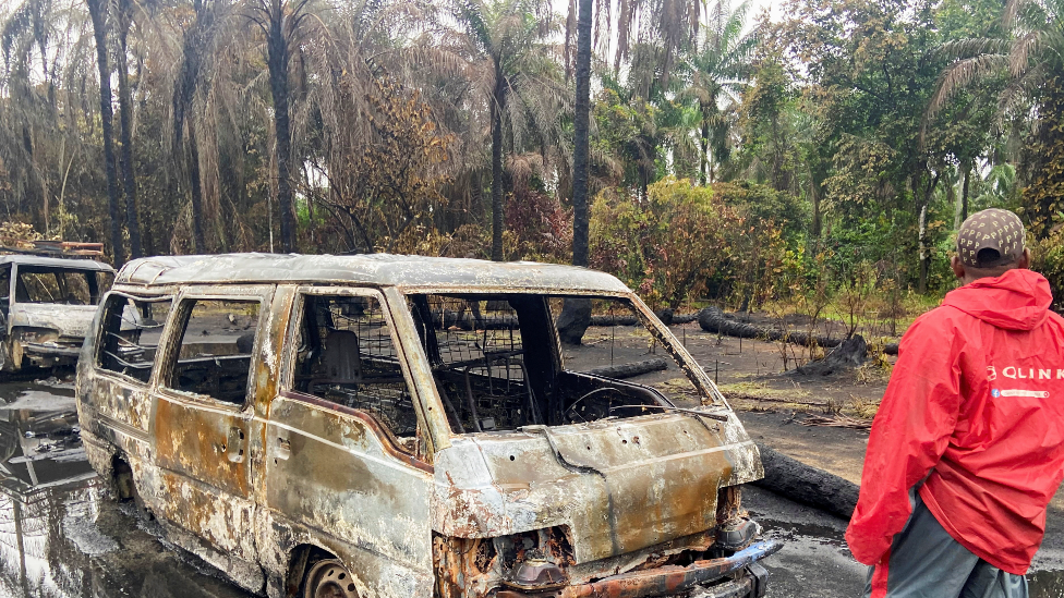 A man near burn-out vehicles after an explosion at an illegal oil refinery in the Niger Delta, Nigeria - April 2022