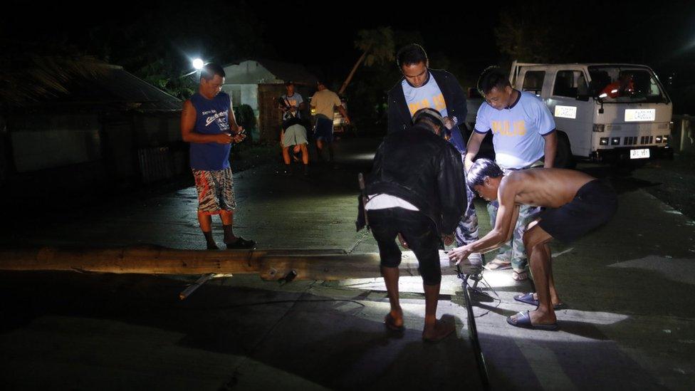 Filipino policemen and villagers clear a toppled post as Super Typhoon Mangkhut approaches the town of Aparri