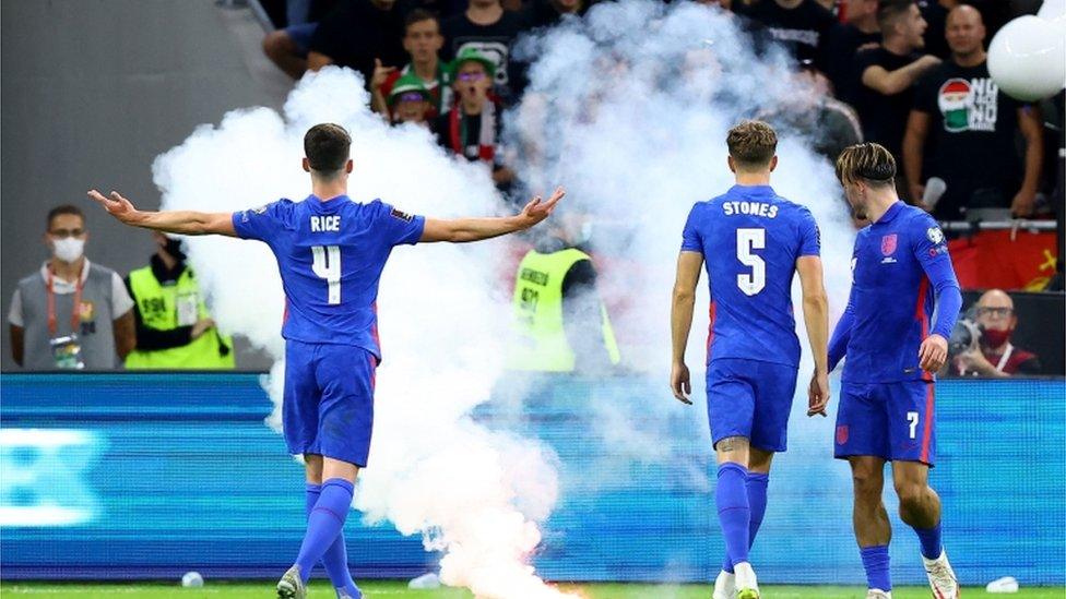 England players react to flare thrown by crowd.