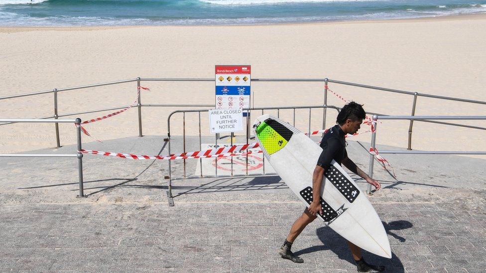 A surfer walks past Bondi Beach which is closed due to coronavirus restrictions