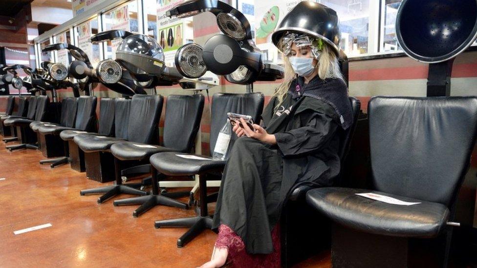 A customer wearing a face mask sits under a dryer at an empty salon in Marietta, Georgia