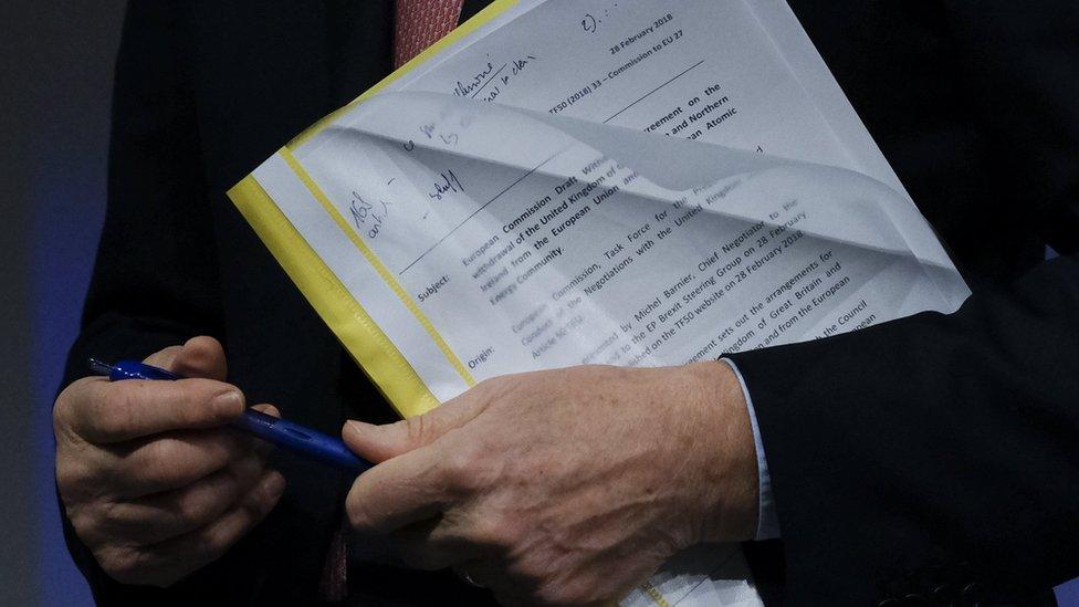 Michel Barnier holding the EU draft withdrawal agreement document in a plastic folder