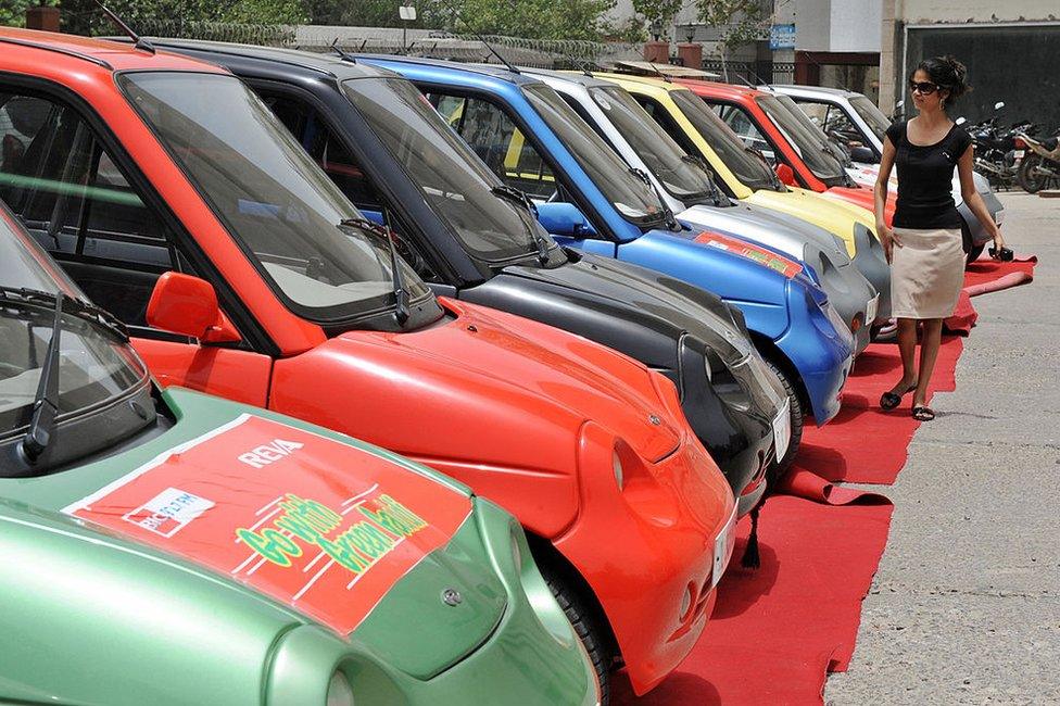 An Indian woman walks past a line of electric Reva motorcars prior to a Reva car rally held to celebrate World Environment Day in New Delhi on June 5, 2009.