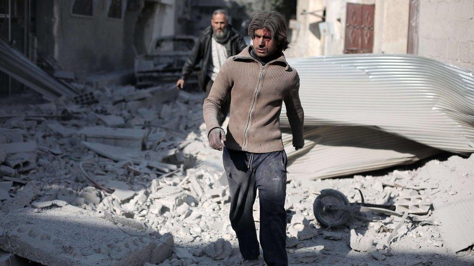 An injured Syrian man walks amid the rubble of destroyed buildings following reported air strikes by government in the eastern Ghouta region (14 December 2015)