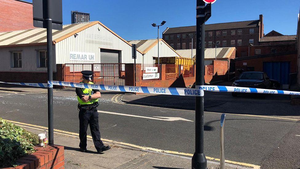 A police officer standing beside a road closed by police cordon tape